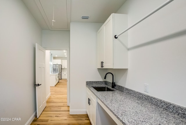 kitchen with light hardwood / wood-style floors, white cabinets, sink, stone counters, and stainless steel fridge