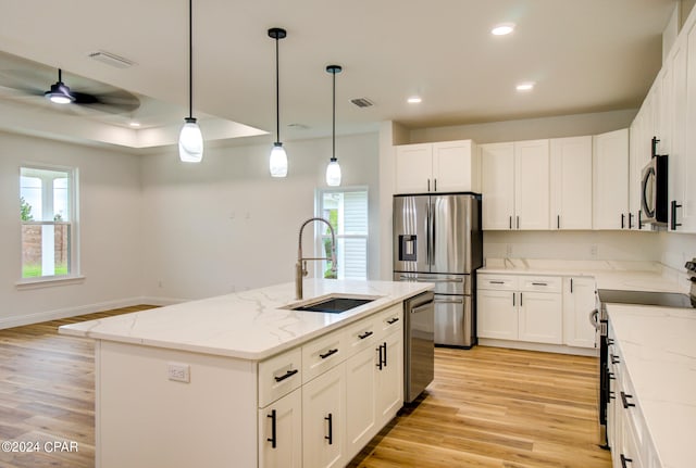 kitchen with white cabinets, light hardwood / wood-style floors, stainless steel appliances, and a center island with sink