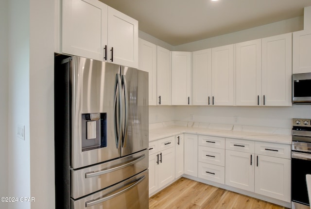 kitchen with white cabinets, light wood-type flooring, stainless steel appliances, and light stone countertops