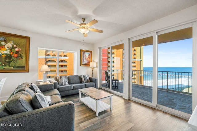 living room with ceiling fan, a textured ceiling, hardwood / wood-style floors, and a water view