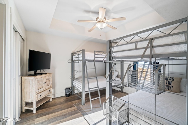 bedroom with a tray ceiling, ceiling fan, dark wood-type flooring, and a closet