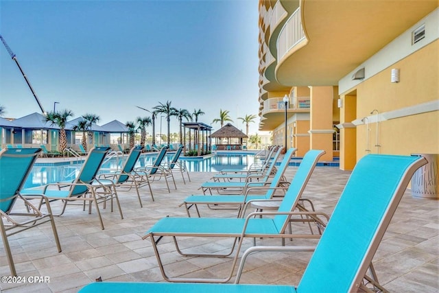 patio terrace at dusk featuring a community pool and a balcony