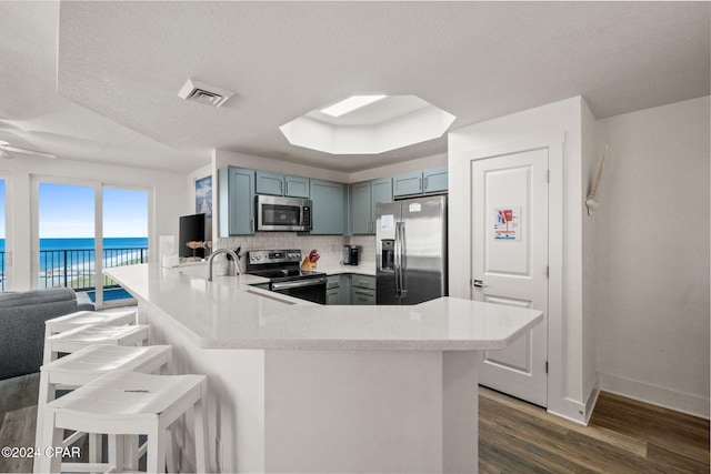 kitchen with appliances with stainless steel finishes, a breakfast bar, kitchen peninsula, a textured ceiling, and dark hardwood / wood-style floors