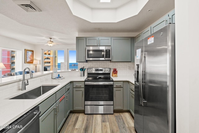 kitchen with decorative backsplash, stainless steel appliances, light wood-type flooring, ceiling fan, and sink