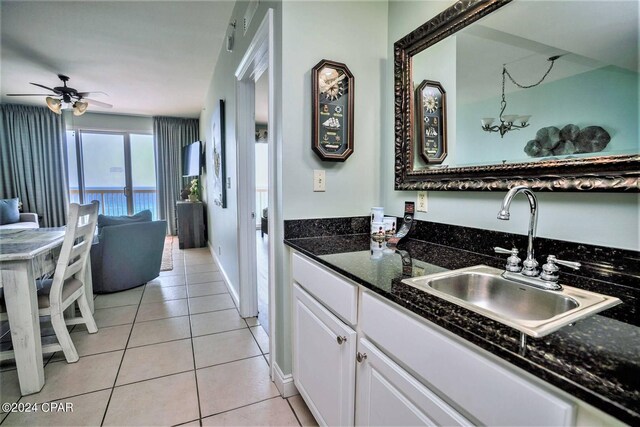 kitchen with sink, dark stone countertops, white cabinets, light tile patterned floors, and ceiling fan