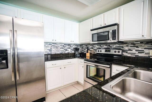 kitchen with appliances with stainless steel finishes, white cabinetry, dark stone countertops, decorative backsplash, and light tile patterned floors