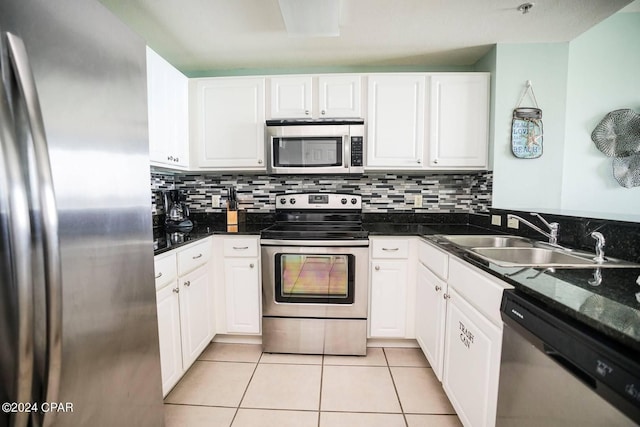 kitchen with sink, white cabinetry, dark stone countertops, light tile patterned floors, and stainless steel appliances