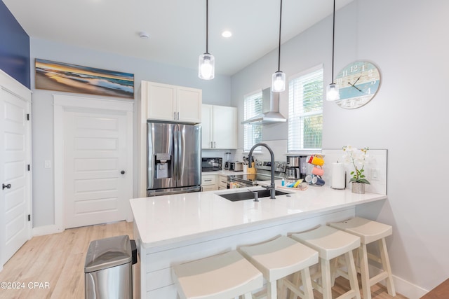 kitchen with kitchen peninsula, stainless steel fridge, wall chimney exhaust hood, pendant lighting, and white cabinets