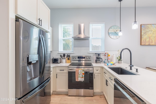 kitchen featuring sink, wall chimney exhaust hood, decorative light fixtures, white cabinetry, and stainless steel appliances