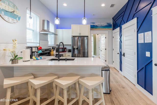 kitchen featuring kitchen peninsula, stainless steel refrigerator with ice dispenser, wall chimney range hood, white cabinetry, and a breakfast bar area