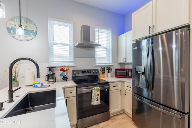 kitchen featuring wall chimney exhaust hood, stainless steel appliances, sink, decorative light fixtures, and white cabinetry