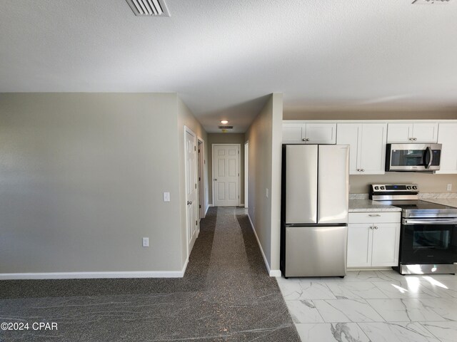 kitchen with marble finish floor, stainless steel appliances, white cabinetry, and baseboards