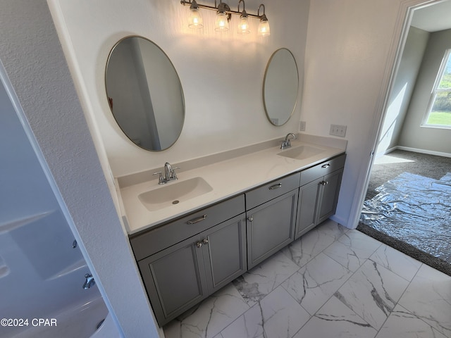 full bath with marble finish floor, double vanity, a sink, and baseboards