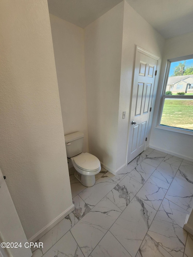 bathroom with marble finish floor, toilet, and baseboards