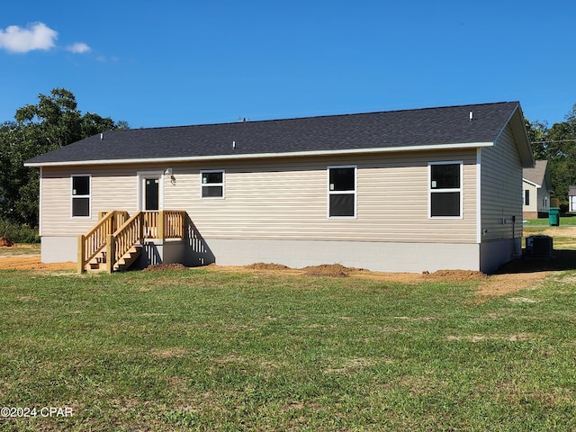 rear view of house featuring a shingled roof, central AC unit, and a lawn