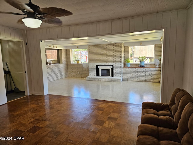 unfurnished living room with ceiling fan, parquet flooring, brick wall, and a brick fireplace