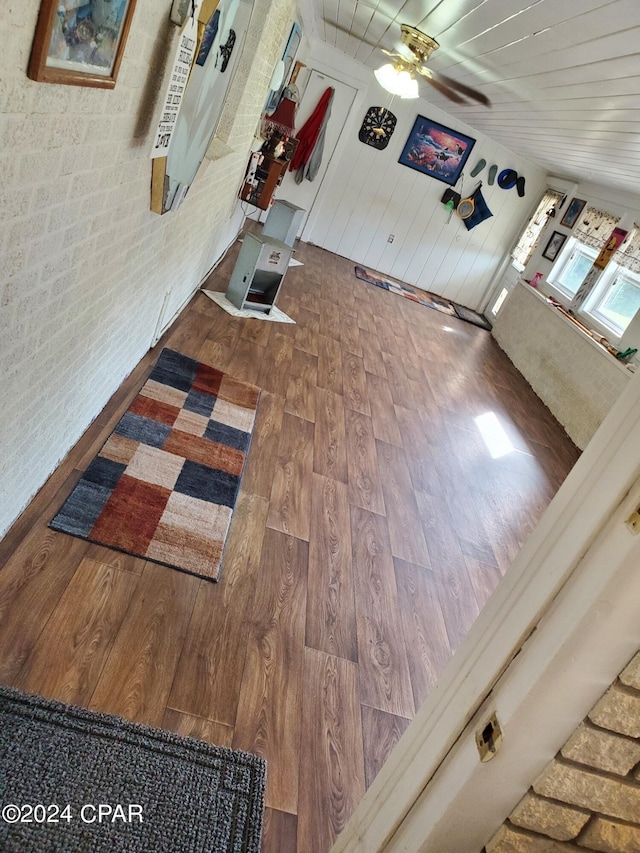 living room with wood-type flooring, water heater, ceiling fan, and brick wall