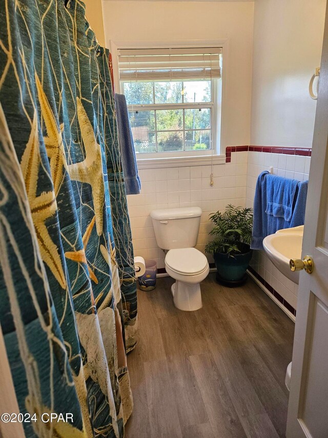 bathroom featuring wood-type flooring, toilet, and tile walls