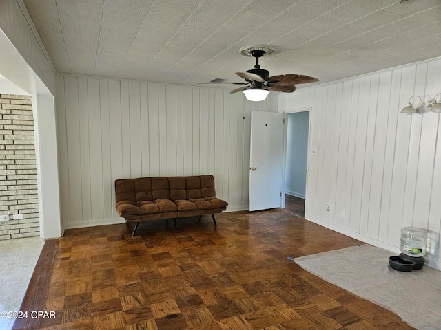 living area with ceiling fan, wooden walls, and dark parquet floors