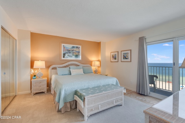 bedroom featuring access to outside, a water view, a textured ceiling, light colored carpet, and a closet