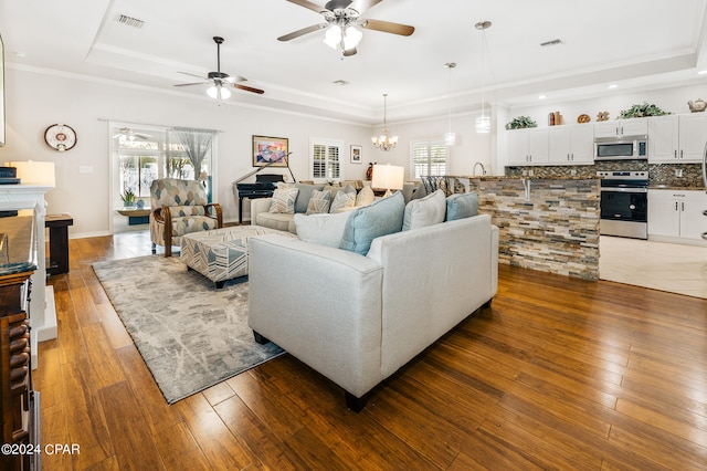 living room featuring ceiling fan with notable chandelier, dark hardwood / wood-style flooring, crown molding, and a tray ceiling