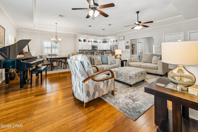 living room with a tray ceiling, hardwood / wood-style flooring, crown molding, and ceiling fan with notable chandelier