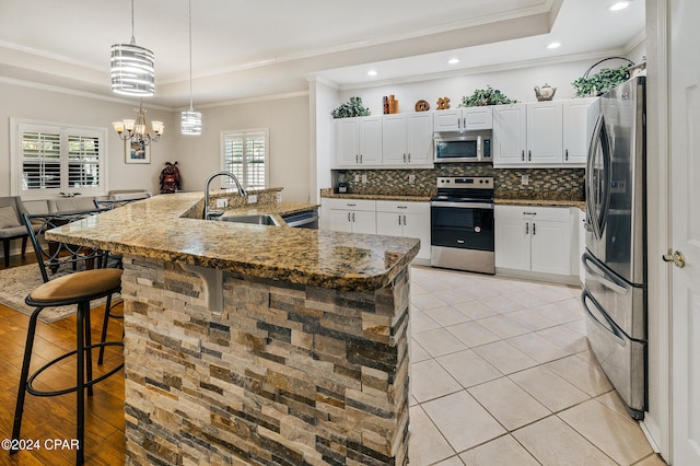 kitchen with stainless steel appliances, white cabinetry, a large island with sink, ornamental molding, and light hardwood / wood-style flooring