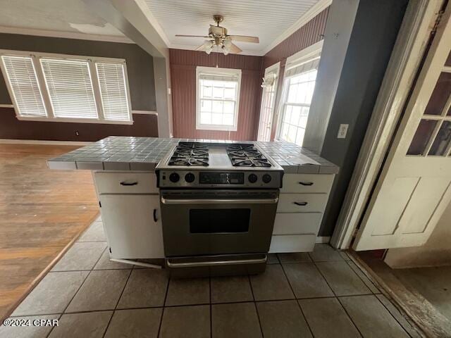 kitchen featuring ceiling fan, stainless steel range with gas cooktop, dark tile patterned floors, tile countertops, and kitchen peninsula