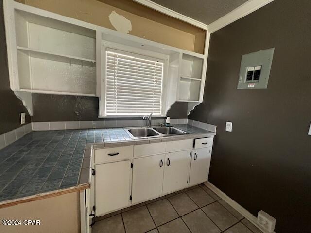 kitchen featuring tile countertops, white cabinets, sink, ornamental molding, and light tile patterned flooring