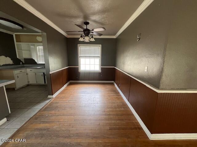 unfurnished dining area with a textured ceiling, ceiling fan, light wood-type flooring, and crown molding