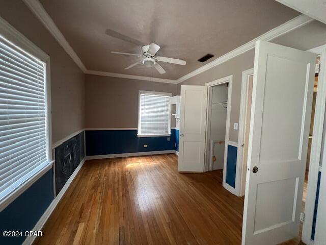 unfurnished bedroom featuring hardwood / wood-style floors, ceiling fan, a spacious closet, and ornamental molding