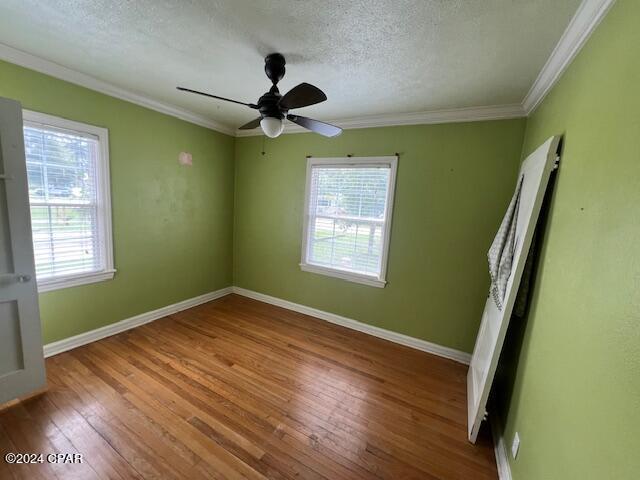 spare room with a healthy amount of sunlight, crown molding, wood-type flooring, and a textured ceiling