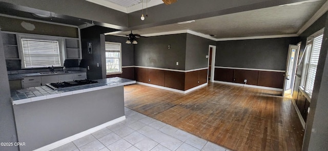 kitchen with ceiling fan, crown molding, light tile patterned floors, tile countertops, and black gas cooktop