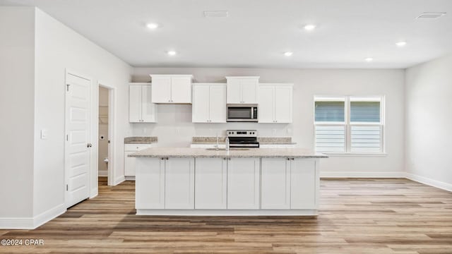 kitchen with light wood finished floors, light stone countertops, white cabinets, stainless steel appliances, and a kitchen island with sink