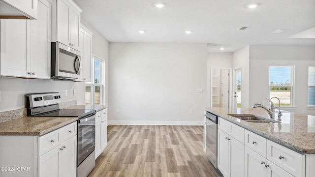 kitchen featuring light wood-style flooring, a sink, stainless steel appliances, baseboards, and light stone countertops