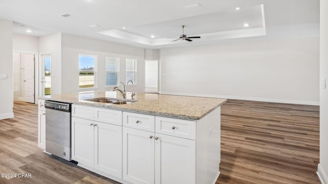 kitchen featuring an island with sink, a sink, stainless steel dishwasher, white cabinetry, and a raised ceiling