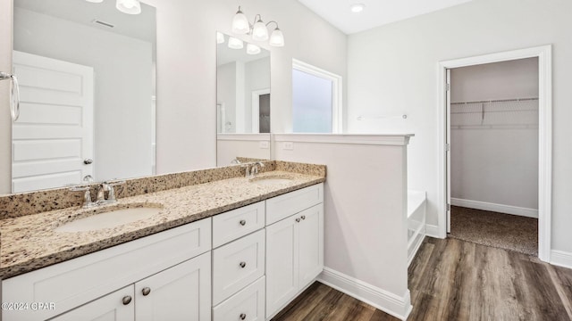 bathroom with wood finished floors, a walk in closet, baseboards, and a sink