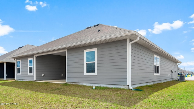 rear view of house featuring central air condition unit, a patio, a yard, and roof with shingles