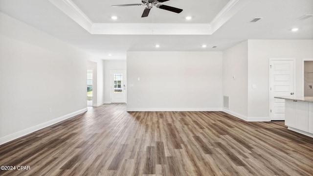 unfurnished living room featuring a tray ceiling, wood finished floors, baseboards, and ornamental molding