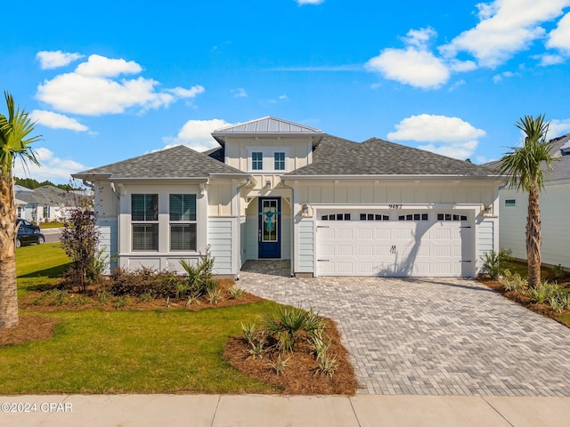 view of front of home with decorative driveway, a shingled roof, an attached garage, board and batten siding, and a front yard