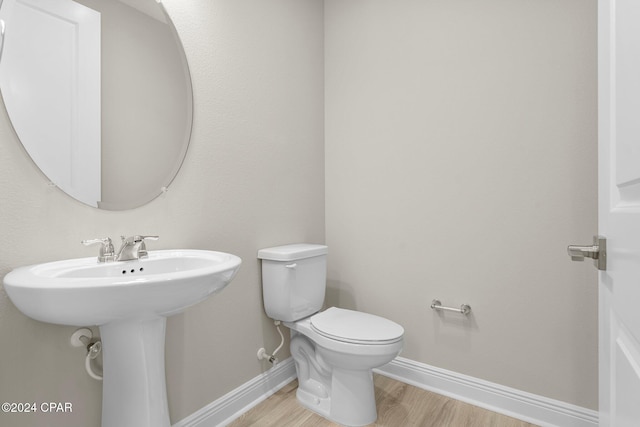 half bathroom with wood finished floors, toilet, and baseboards