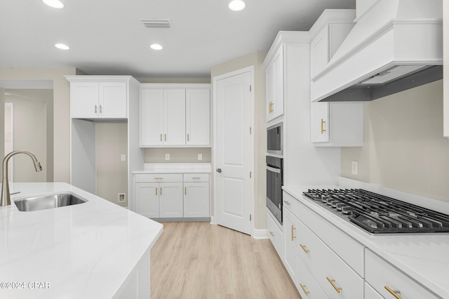 kitchen featuring custom range hood, oven, stainless steel gas stovetop, white cabinetry, and a sink