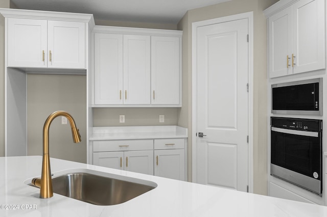 kitchen featuring wall oven, white cabinetry, light countertops, and a sink