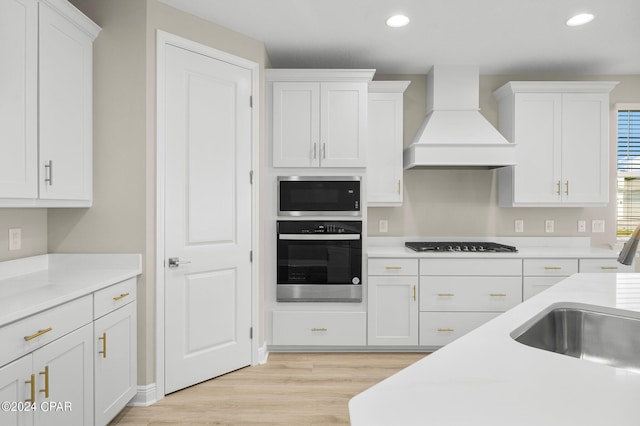 kitchen with black stovetop, white cabinets, stainless steel oven, built in microwave, and premium range hood