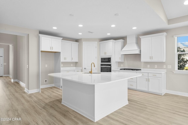 kitchen featuring a kitchen island with sink, a sink, premium range hood, baseboards, and black appliances
