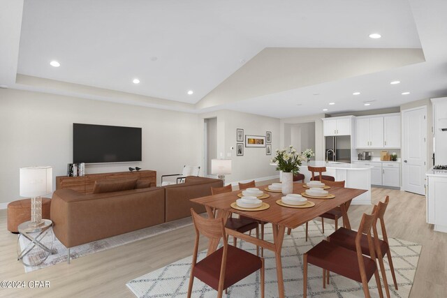 dining area with sink, light hardwood / wood-style floors, and high vaulted ceiling