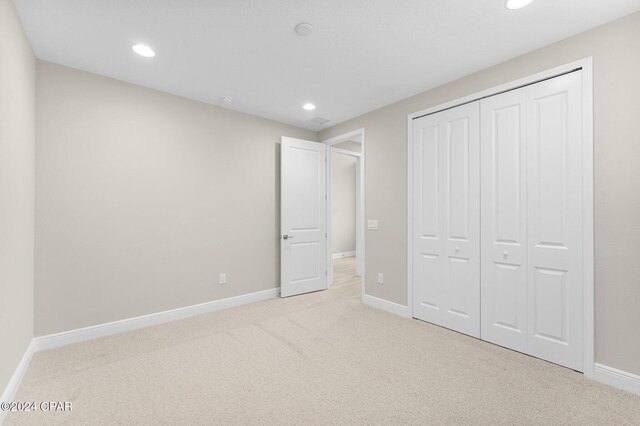 unfurnished bedroom with light colored carpet and a closet