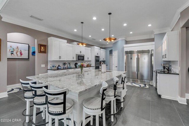 kitchen featuring decorative light fixtures, white cabinetry, stainless steel appliances, dark stone countertops, and a large island