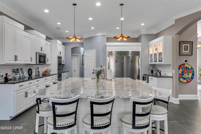 kitchen with decorative light fixtures, a large island with sink, appliances with stainless steel finishes, and white cabinetry