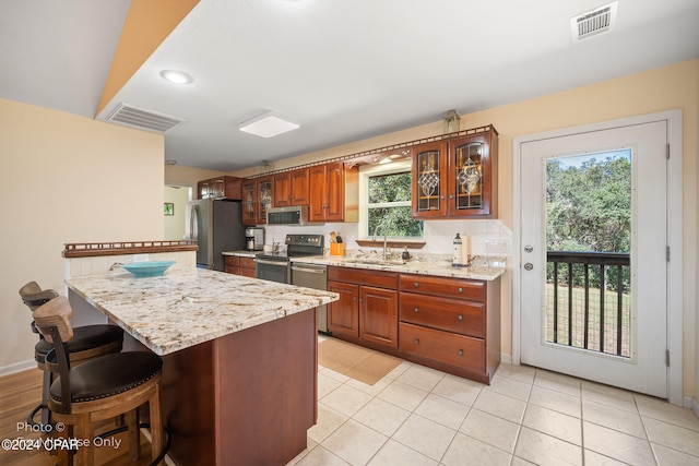 kitchen with light stone countertops, a center island, sink, light tile patterned floors, and appliances with stainless steel finishes